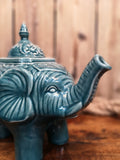 Zoom sur la théière bleue en céramique, en forme d’éléphant, mesure environ 11" de long sur 8,5" de hauteur, couvercle et trompe compris.